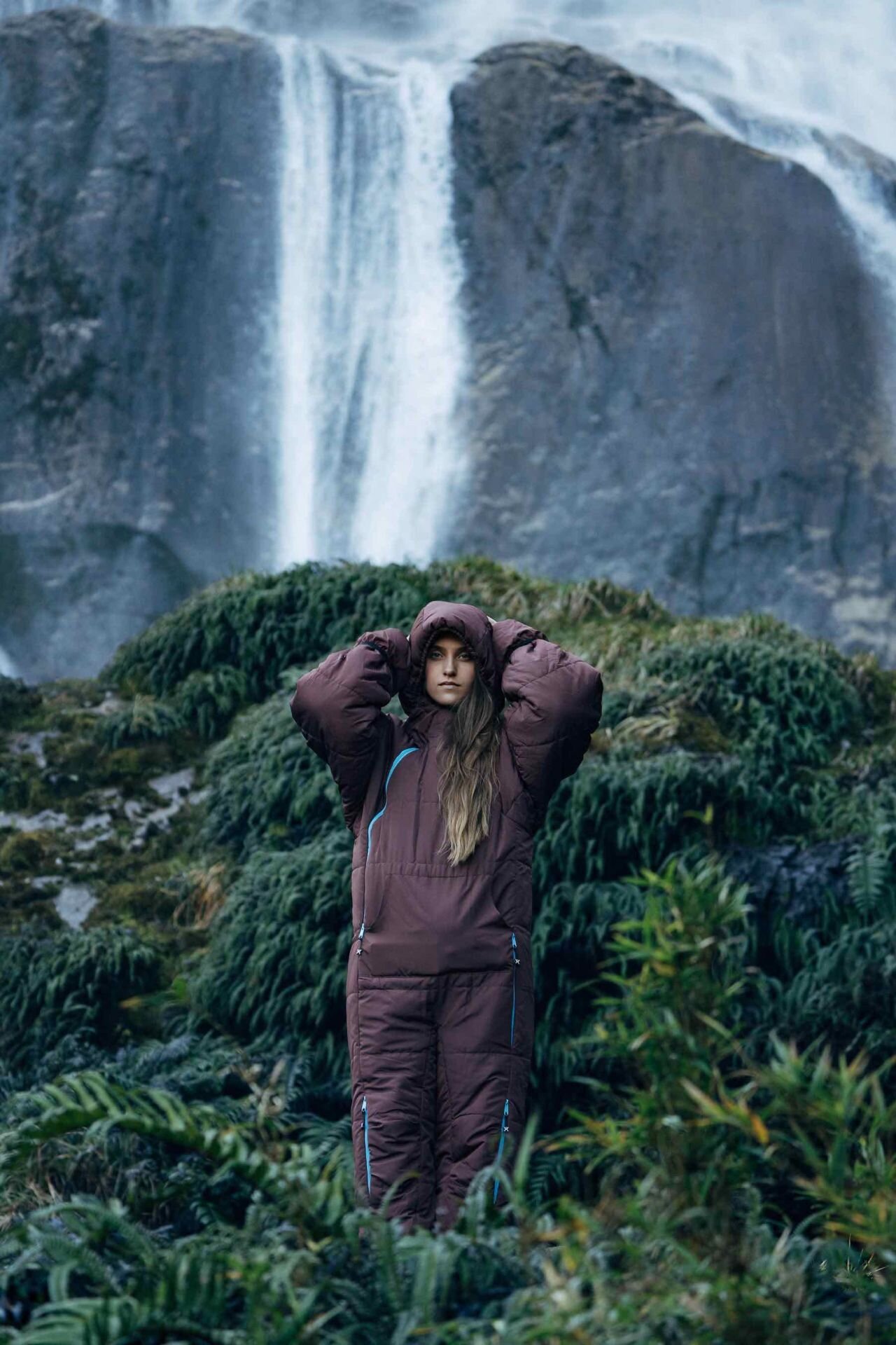 junge Frau steht in ihrem tragbaren Schlafsack von Selkbag vor einem Wasserfall